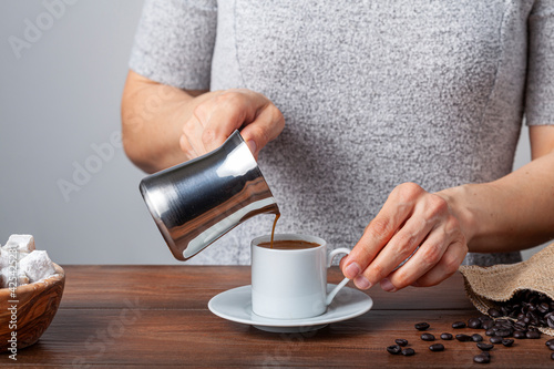 Traditional Turkish coffee served in classical cups with Turkish delights. A metal coffee pot is in the background. A woman is pouring coffee to the cup. photo