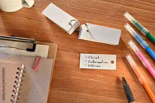There is a a word card with chief information officer written on it. They are on the desk along with stationery such as notebooks and colored pens.