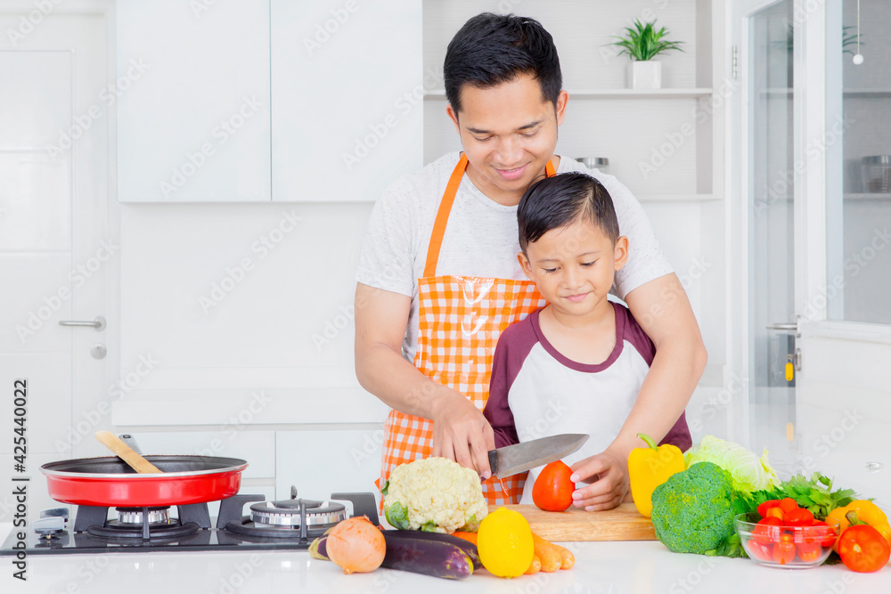 Happy father teaching his son to slicing a tomato Happy father teaching his son to slicing a tomato