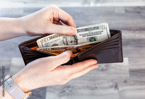 Person’s hand taking 20 dollar banknotes from brown leather wallet, paying cash for shopping. Pocket money for daily life spend. Person hold money from purse. Currency for worldwide business concept photo