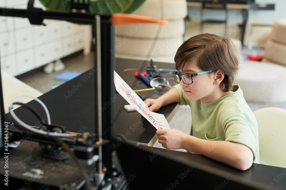 High angle portrait of little boy using 3D printer during engineering and robotics class at modern school, copy space High angle portrait of little boy using 3D printer during engineering and robotics class at modern school, copy space