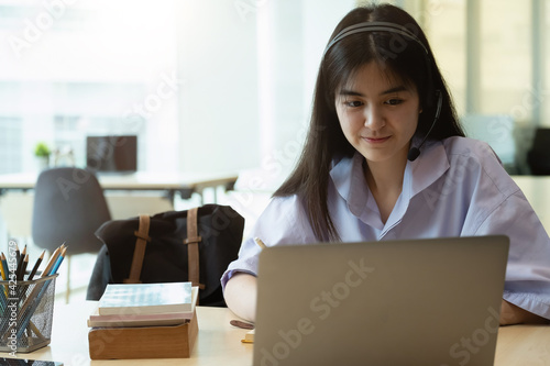 Portrait of a beautiful asian young woman studying while sitting at the table with laptop computer and notebook at home - elearning concept.