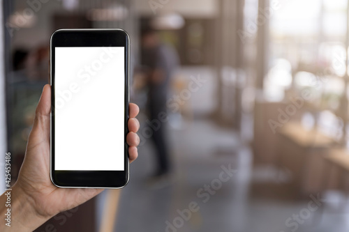 Hand man holding black mobile phone with blank white screen with blur coffee shop background. Mockup image of hand holding smartphone with blank white screen with copy space
