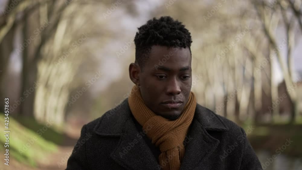 Contemplative man walking outside at park during winter wearing coat and scarf Contemplative man walking outside at park during winter wearing coat and scarf