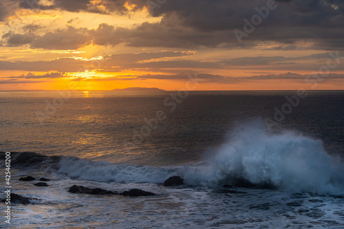 Beautiful view of the ocean waves chasing in rocks with a magical sunset in the horizon