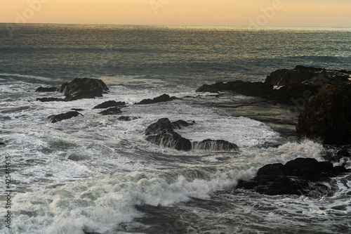Beautiful view of the ocean waves chasing in rocks with a magical sunset in the horizon