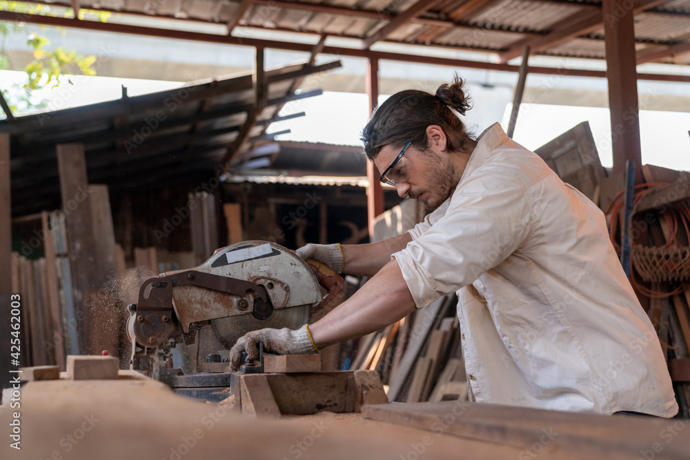 Caucasian carpenter wearing a safety goggle and cutting wood on a table saw in a carpentry shop. Woodworker sawing wood with circular saw tools in the workshop. Woodcraft industrial and Hobby concepts