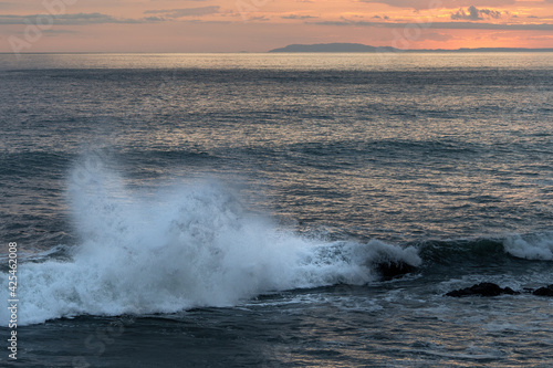 Beautiful view of the ocean waves chasing in rocks with a magical sunset in the horizon