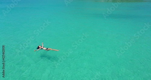 Aerial: A woman swims in blue sea water in the bay. Nature and relaxation, top view. 