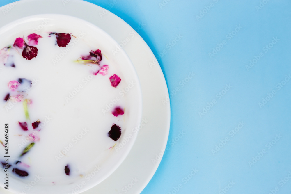 Fototapeta premium White Cup with vegan milk and flowers on a blue background. Concept of vegetarian drinks and food, herbal teas, beauty and health, Spa