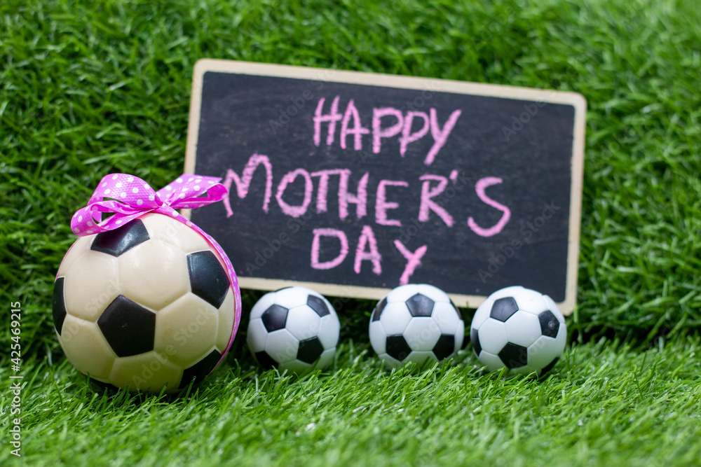 Obraz premium Soccer ball for mother's day with ball and pink ribbon on green grass with word