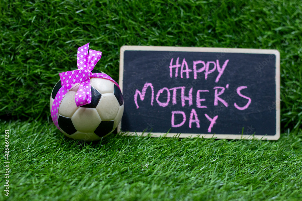 Obraz premium Soccer ball for mother's day with ball and pink ribbon on green grass with word
