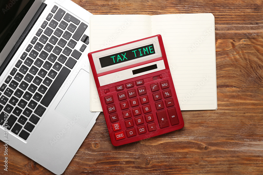 Modern calculator with text TAX TIME and laptop with notebook on wooden background Modern calculator with text TAX TIME and laptop with notebook on wooden background