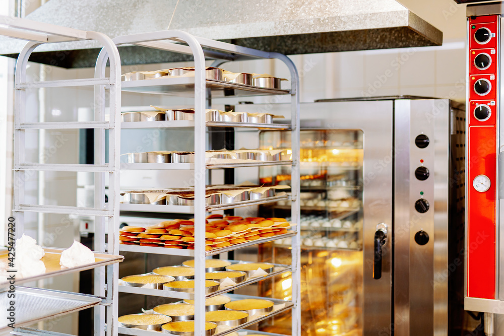 trolley with freshly baked cakes and pastries for the production of desserts. Confectionery production and factory. Baking oven on the background. trolley with freshly baked cakes and pastries for the production of desserts. Confectionery production and factory. Baking oven on the background.