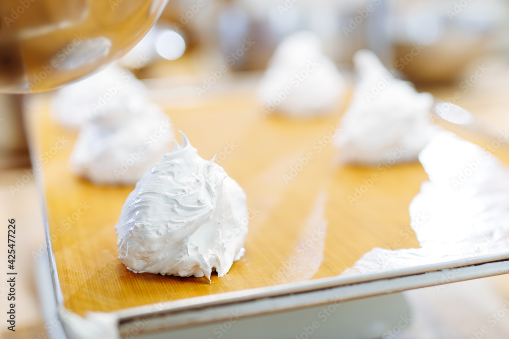 the pastry chef squeezes cream on the non-stick baking sheet. cream on meringue. preparation of dessert on confectionery factory . the pastry chef squeezes cream on the non-stick baking sheet. cream on meringue. preparation of dessert on confectionery factory .