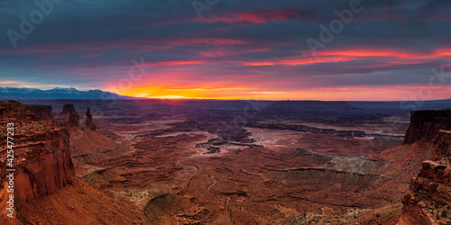 Panoramic view above Mesa Arch towards Washer Woman Arch and the La Sal Mountains under a fiery sunrise