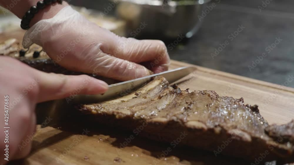 Cutting beef ribs on wooden cut board at meat tasting event. Close up on chef hands. Slow motion shot. Cutting beef ribs on wooden cut board at meat tasting event. Close up on chef hands. Slow motion shot.