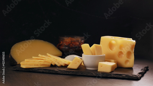 Several types of yellow cheese in chunks and cut into slices on black background.