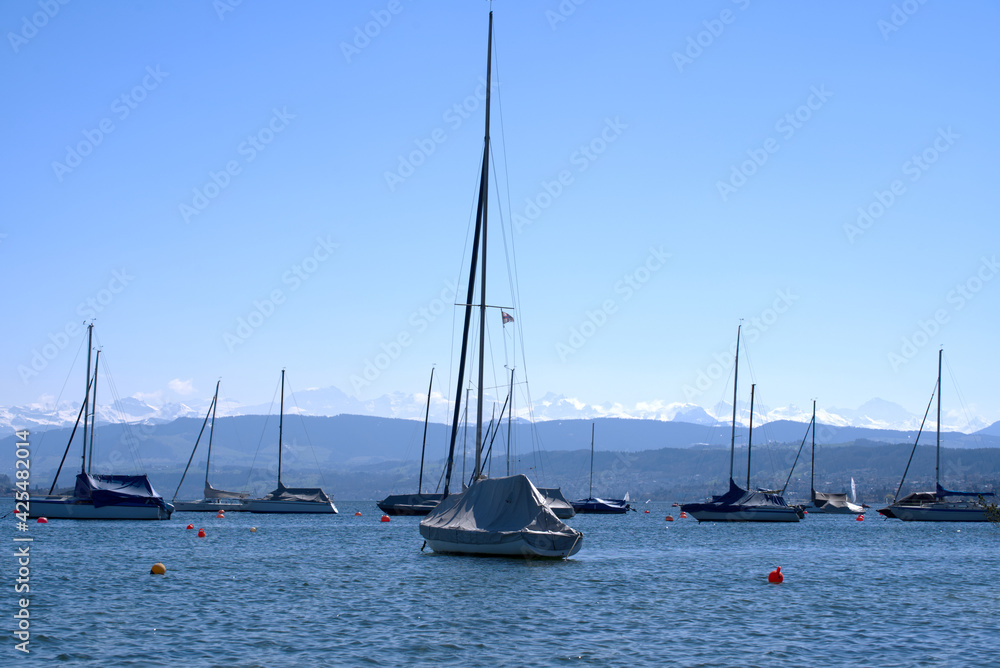 Lake Zurich at springtime with sailing boats with blue sky and snow capped mountains in the background. Photo taken April 4th, 2021, Zurich, Switzerland.