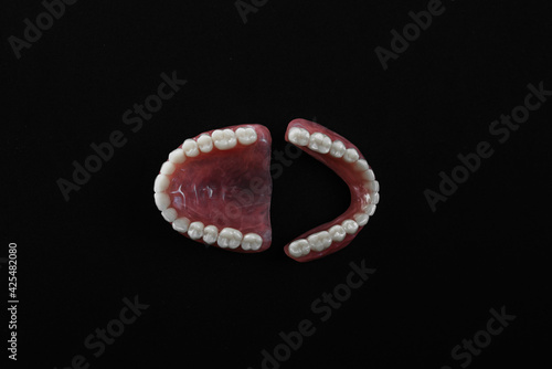 Full removable plastic denture of the jaws. A set of dentures on a black background. Two acrylic dentures. Upper and lower jaws with fake teeth. Dentures or false teeth  close-up. Copy space