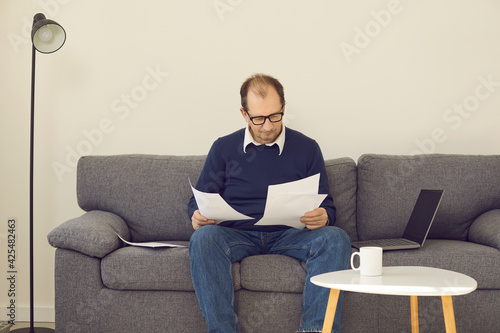 Pensive mature businessman freelancer brainstorming working on new project looking at stock growth charts reading paper documents in comfortable home office. Remote work, online business, ecommerce