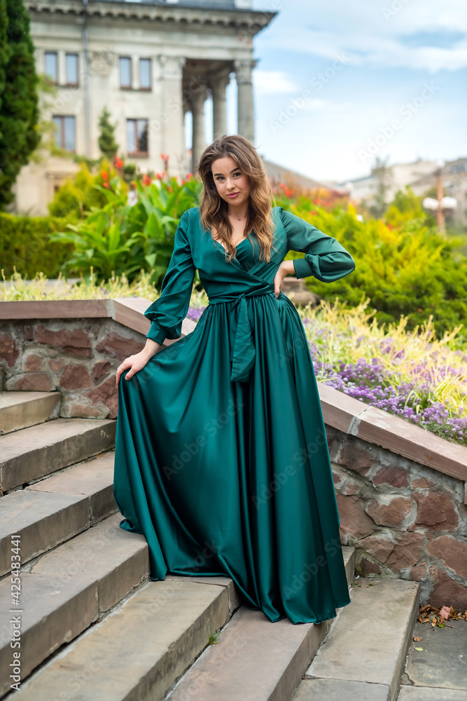 beautiful sensual girl wearing long elegant green dress standing on the building steps