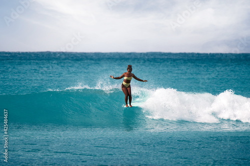 Charming curly African-American dark-skinned young woman, professional surfer do noseride on a long surfboard 