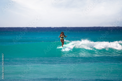 Charming curly African-American dark-skinned young woman, professional surfer do noseride on a long surfboard 