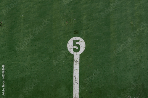 fronton wall in the Basque ball sport, in which the game marks are painted with the number 5 painted in negative in a white circle on a green background © Javier Peribáñez