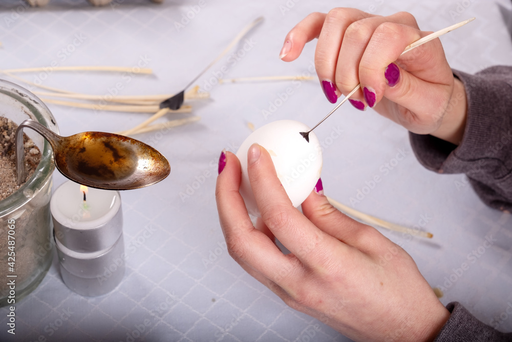 Female hands paints a white Easter egg according to german Sorbian tradition with a trimmed goose quill and melted wax.