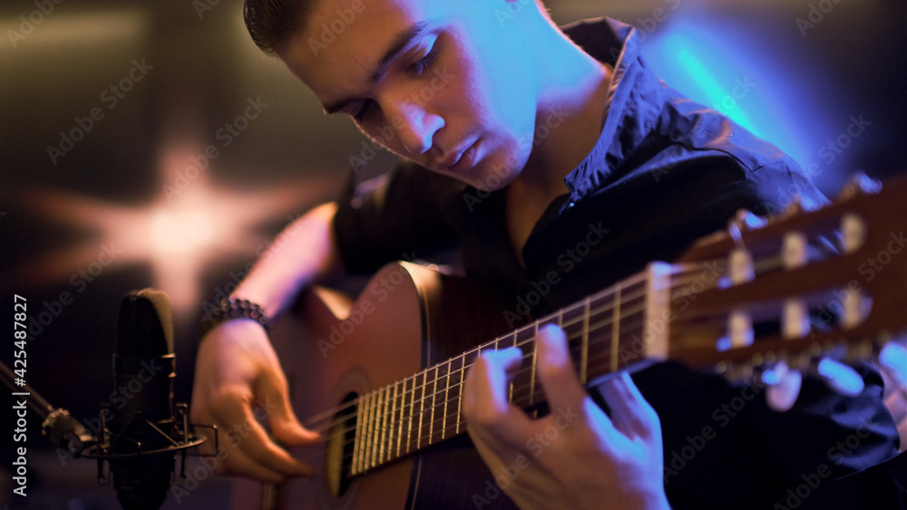 Obraz premium Man plays guitar. Young man plays a musical instrument. Musician records his composition in a music Studio using professional microphone
