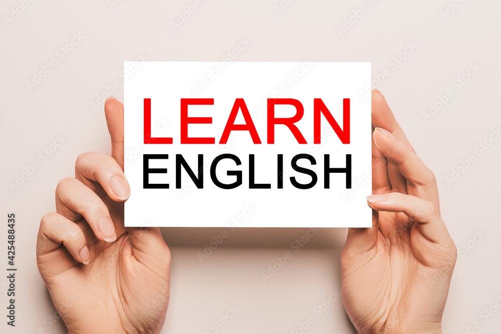 Female hands hold card paper with text Learn ENGLISH on a yellow background. Education and language concept Female hands hold card paper with text Learn ENGLISH on a yellow background. Education and language concept