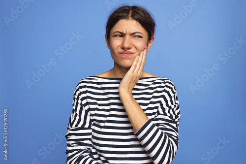 Frustrated unhappy teenage girl having pain in wisdom tooth, holding hand on her cheek, making painful grimace, being afraid of dentists. Stressed young woman trying to tolerate toothache © Anatoliy Karlyuk