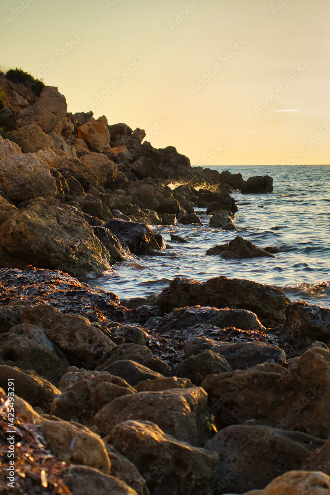 Water splashing behind a rock at Golden Bay, Malta at sunset.