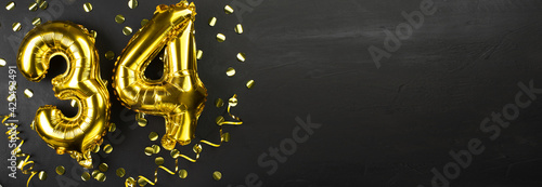 golden foil balloon number thirty four. Birthday or anniversary card with the inscription 34. Black concrete background. Anniversary celebration. Banner. photo