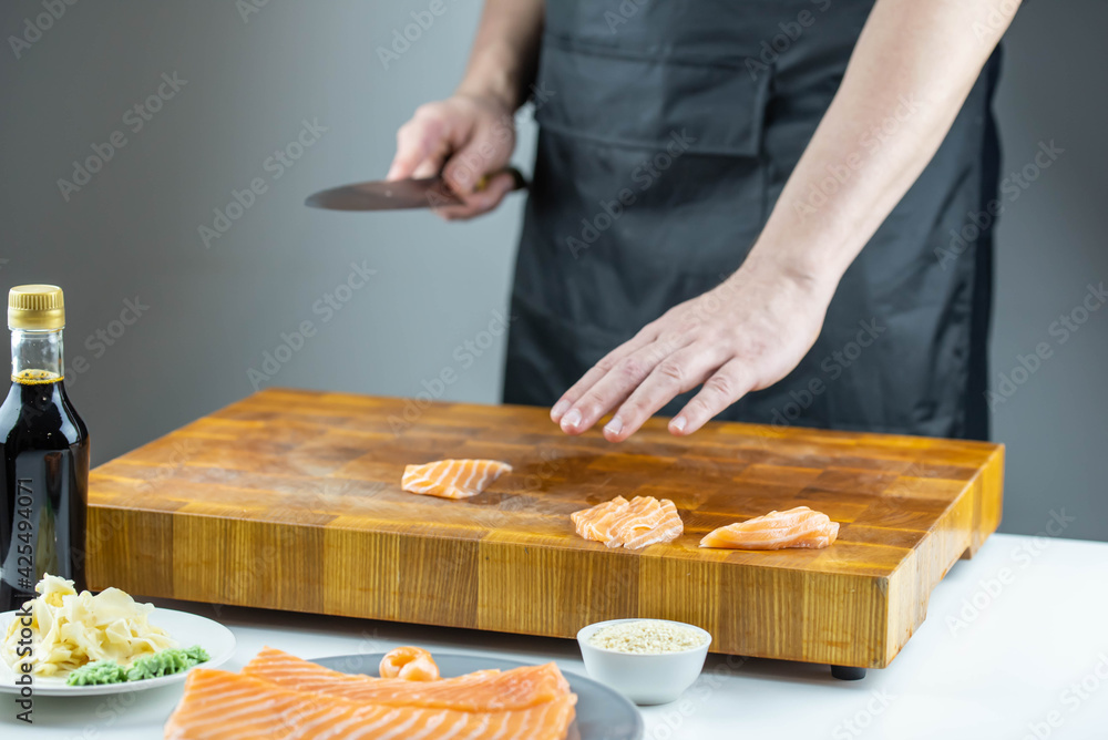 Close up of Chef cook hands chopping salmon fish for traditional Asian cuisine with Japanese knife. Professional Sushi chef cutting seafood for rolls.