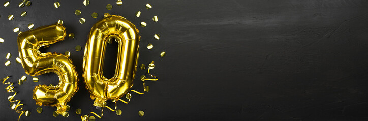 golden foil balloon number fifty. Birthday or anniversary card with the inscription 50. Black concrete background. Anniversary celebration. Banner.
