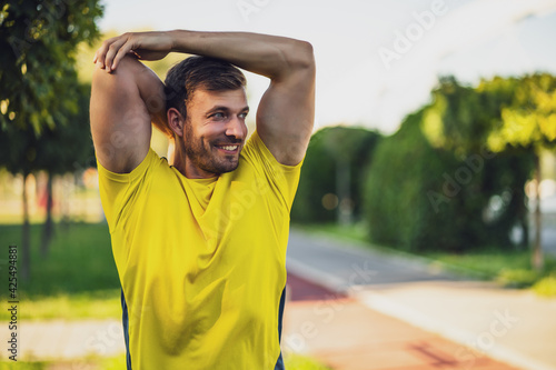 Young man is exercising outdoor. He is stretching his body and warming up for jogging.