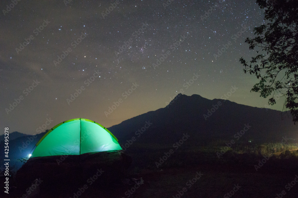 Camping fire under the amazing blurr starry sky with a lot of shining stars and clouds. Travel recreational outdoor activity concept. 