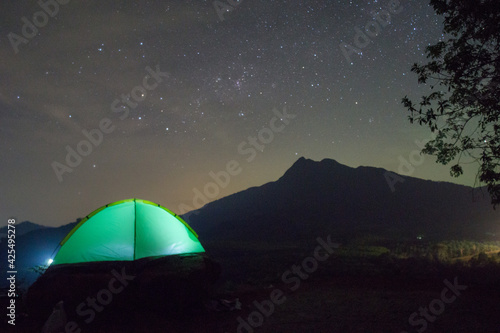 Camping fire under the amazing blurr starry sky with a lot of shining stars and clouds. Travel recreational outdoor activity concept. 