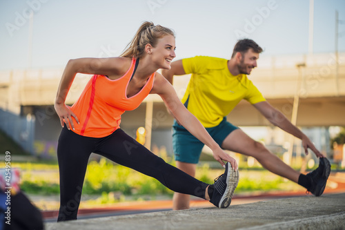 Young couple is exercising outdoor. They are and stretching and warming up for jogging.