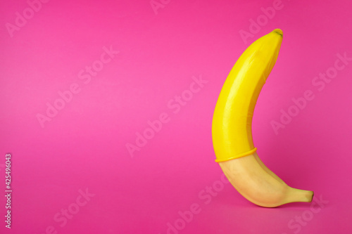 Banana with yellow condom on pink background