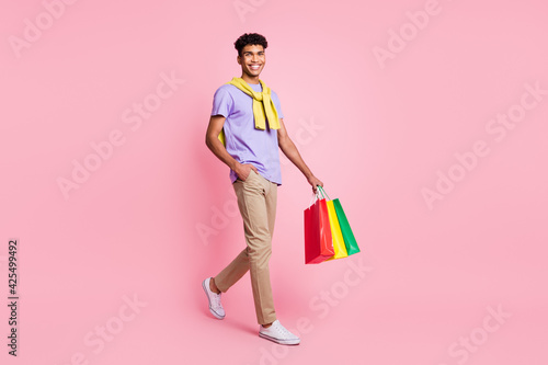 Full size profile side photo of young man happy positive smile go walk shopping bag sale isolated over pink color background