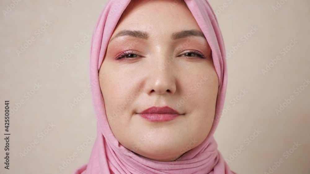 Young muslim woman in pink headscarf raise head and smiles looking at camera. Young muslim woman in pink headscarf raise head and smiles looking at camera.