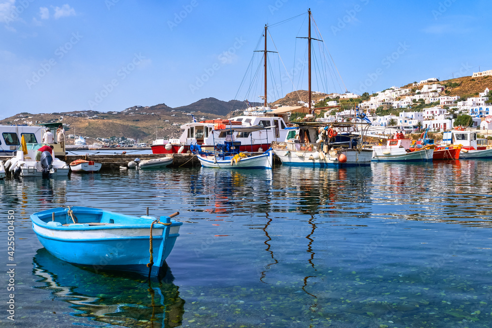Beautiful summer day in typical marina of Greek island. Fishing boats, yachts by jetty. Whitewashed houses. Small boat. Mykonos, Cyclades, Greece.