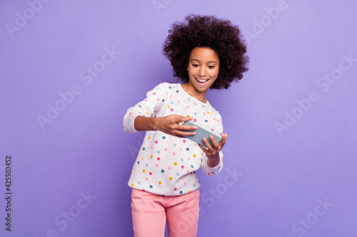Photo portrait of small girl playing video games on cellphone smiling isolated on pastel purple color background