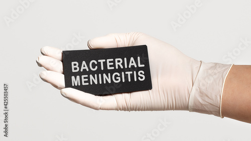 Closeup of the hand in a white sterile glove holding a card with words - Bacterial Meningitis