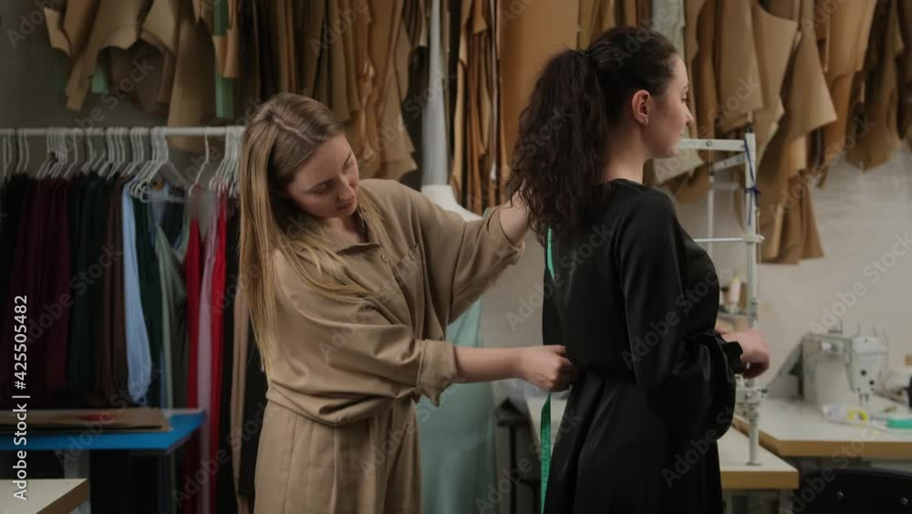 Femail seamstress taking measurements of female client using tape in atelier. Two women in tailoring studio working together. Designer and model prepairing to fashion show measuring size for dress. Femail seamstress taking measurements of female client using tape in atelier. Two women in tailoring studio working together. Designer and model prepairing to fashion show measuring size for dress.