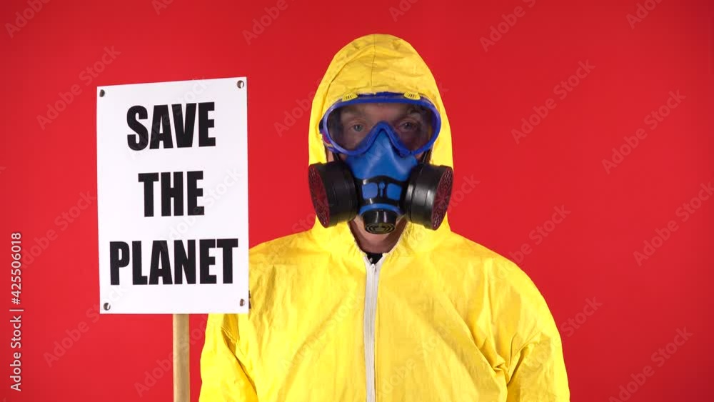 A man in a protective yellow suit and chemical mask, with a poster Save the planet affirmatively nods his head. Isolate, studio shooting. The concept of saving the planet A man in a protective yellow suit and chemical mask, with a poster Save the planet affirmatively nods his head. Isolate, studio shooting. The concept of saving the planet