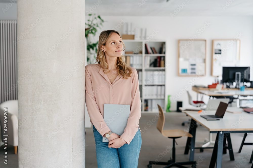 Thoughtful young businesswoman standing daydreaming in a spacious office Thoughtful young businesswoman standing daydreaming in a spacious office